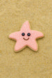 3.25 inch Folk Star or Starfish Metal Cookie Cutter shaped cookie with pink icing and a smiley face on sand.