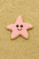 3.25 inch Folk Star or Starfish Metal Cookie Cutter shaped cookie with pink icing and a smiley face on sand.