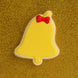 Yellow bell-shaped cookie with a red bow on a gold glittery background from a 3.25 inch Folk Bell Metal Cookie Cutter