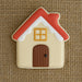 House-shaped cookie with red roof, beige body, and brown door on a textured brown background from a 3.5 inch Gingerbread House Metal Cookie Cutter