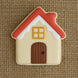 House-shaped cookie with red roof, beige body, and brown door on a textured brown background from a 3.5 inch Gingerbread House Metal Cookie Cutter