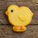 Yellow chick-shaped cookie with orange feet and black eye on a wooden surface from a 2.5 inch Chick Metal Cookie Cutter