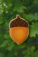 Acorn-shaped cookie with brown cap and orange body on green leaves from a 2.75 inch Acorn Metal Cookie Cutter