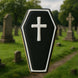 Black coffin-shaped cookie with a white cross on a blurred cemetery background from a 4 inch Coffin Metal Cookie Cutter