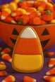 Halloween-themed cookie with candy corn design in front of a bowl of candy corn from a 3 inch Candy Corn Metal Cookie Cutter