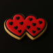 Two heart-shaped cookies with red icing and black heart decorations on a black  background from a 3.5 inch Double Heart Metal Cookie Cutter