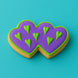 Heart-shaped cookie with purple icing and green heart decorations on a teal background from a 5 inch Double Heart Metal Cookie Cutter