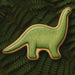 Green dinosaur-shaped cookie on a green leafy background from a 6 inch Brontosaurus Metal Cookie Cutter