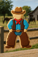 Decorative cookie shaped like a cowboy with a background of a barn and horses from a 4.25 inch Cowboy Metal Cookie Cutter