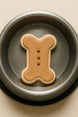 2 inch Mini Dog Bone Metal Cookie Cutter shaped cookie on a silver pet food bowl.