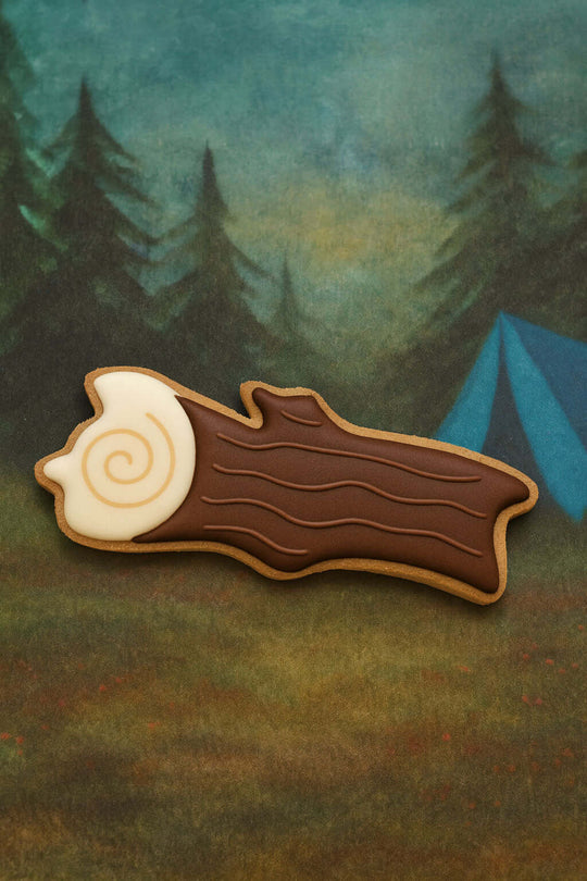 Cookie shaped like a log with a spiral design on a forest background from a 5 inch Camping Log Stick Metal Cookie Cutter