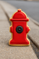 3 inch Fire Hydrant Metal Cookie Cutter shaped cookie in red and black icing on a sidewalk.
