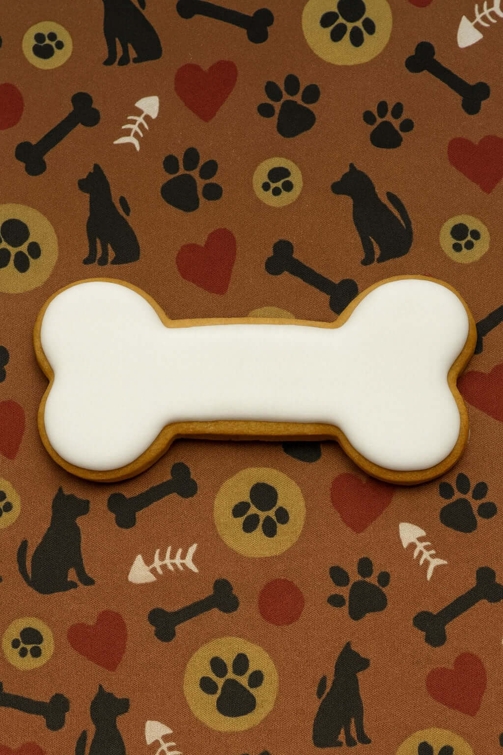 Bone-shaped cookie with white icing on a brown background with dog-themed patterns from a 4 inch Curved Dog Bone Metal Cookie Cutter