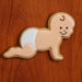 Cookie shaped like a crawling baby with a face on a wooden surface from a 5 inch Crawling Baby Metal Cookie Cutter