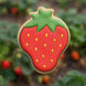 Strawberry-shaped cookie with red body, green leaves, and yellow seeds against a blurred natural background from a 2.5 inch Strawberry Metal Cookie Cutter
