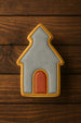 3.5 inch School House Metal Cookie Cutter shaped cookie decorated in gray and orange on a wooden background.