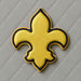 Yellow and black fleur-de-lis design on a gray quilted background from a 4.5 inch Fleur de Lis Metal Cookie Cutter