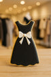 Cookie shaped like a black dress with a white bow on a wooden surface from a 4.75 inch Dress Metal Cookie Cutter