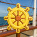 4 inch Ship's Wheel Metal Cookie Cutter shaped cookie in bright yellow and brown with ocean in background.