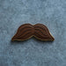 Brown mustache-shaped cookie on a gray textured background from a 5 inch Mustache Metal Cookie Cutter
