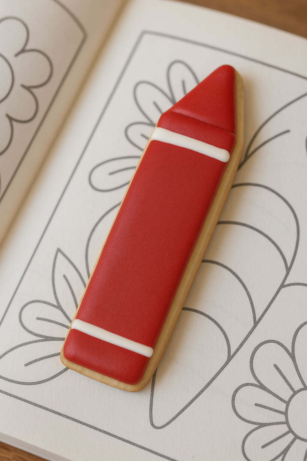 5 inch Crayon Pencil Metal Cookie Cutter shaped cookie resting on a coloring book page.