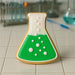 4 inch Beaker Metal Cookie Cutter shaped cookie with green icing and bubbles on a tiled surface.