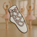 Cookie with a design of a ballet shoe and pink bow, set against a blurred background of ballerinas from a4 inch Ballet Slipper Metal Cookie Cutter