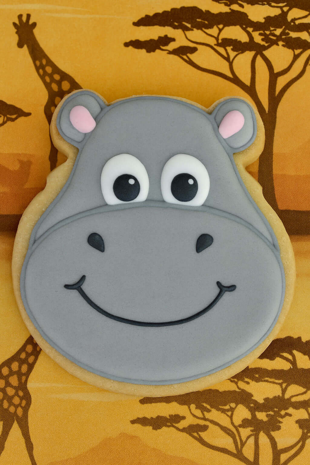 Hippo-shaped cookie with a cartoon face on a background with giraffes and trees FROM A 4.5 inch Hippopotamus Face Metal Cookie Cutter