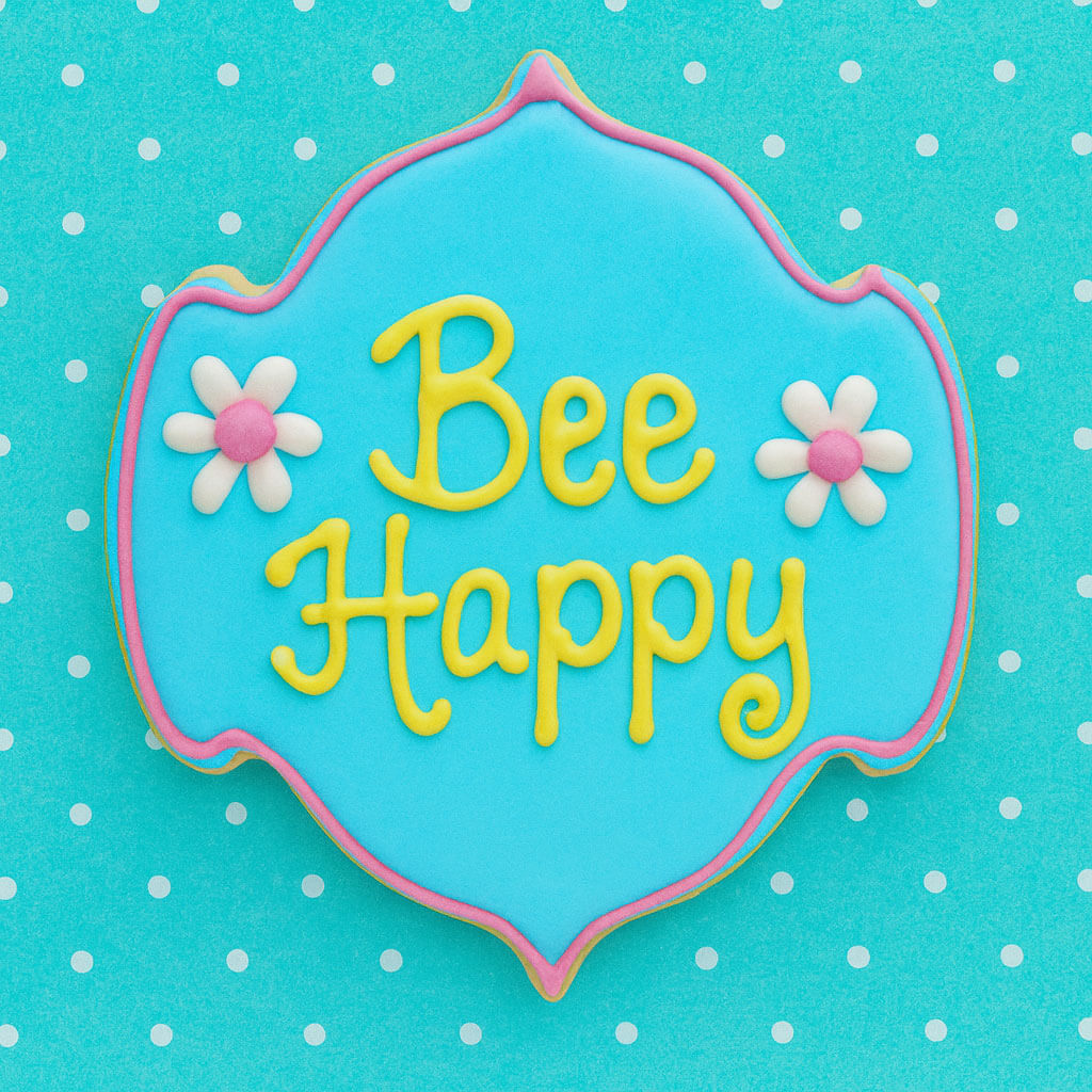 Decorative cookie with 'Bee Happy' text on a blue background with white polka dots from a 5 inch Plaque or Frame Metal Cookie Cutter