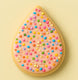 Teardrop-shaped cookie with pink frosting and colorful sprinkles on a light yellow background from a 3.5 inch Tear Drop Rain Flower Petal Metal Cookie Cutter