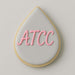 Teardrop-shaped cookie with 'ATCC' in pink icing on a light gray background from a 4 inch Tear Drop Rain Flower Petal Metal Cookie Cutter