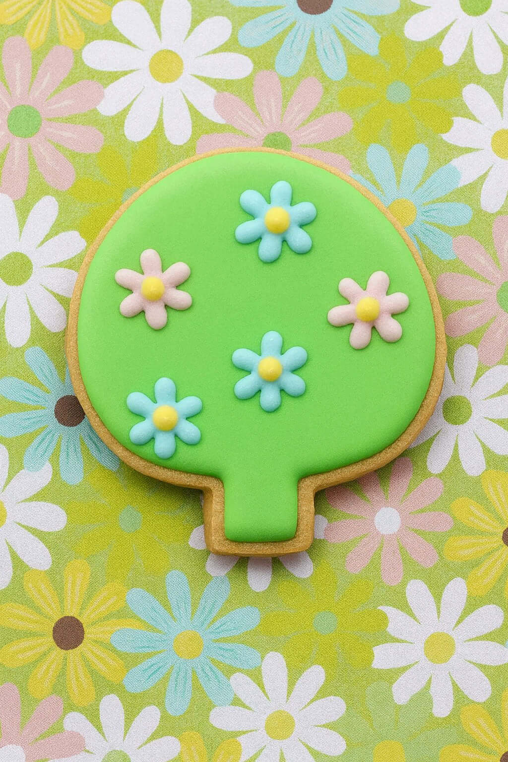 Decorative cookie with green top and floral designs on a floral background from a 4 inch Leaf Tree Shrub Metal Cookie Cutter