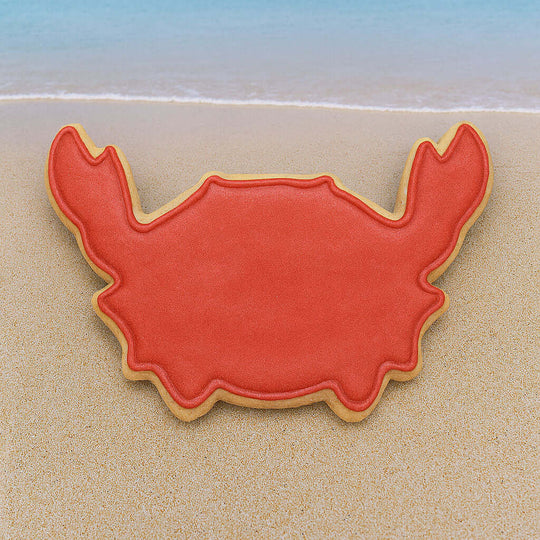 Red crab-shaped cookie on a sandy beach with blue water in the background from a 2.25 inch Mini Crab Metal Cookie Cutter