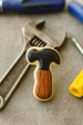 Cookie with a hammer design on a surface with tools in the background from a 2 inch Mini Hammer Metal Cookie Cutter