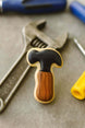 Cookie with a hammer design on a surface with tools in the background from a 2 inch Mini Hammer Metal Cookie Cutter