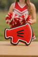 Red and black cookie shaped like a megaphone on a wooden surface with a blurred cheerleader in the background from a 2 inch Mini Megaphone Metal Cookie Cutter