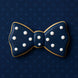 Navy blue bow tie cookie with white dots on a dark blue polka dot background from a 1.75 inch Mini Bow Tie Metal Cookie Cutter