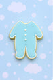 Cookie shaped like a baby footie pajamas on a light blue background with white dots from a  2 inch Mini Footie Pajamas Metal Cookie Cutter