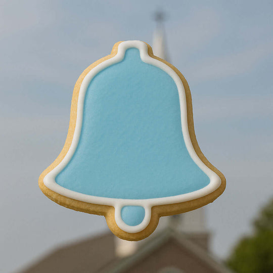3.5 inch Bell Metal Cookie Cutter cookie decorated in blue icing, shaped like a bell against a blurred background.