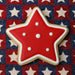 Star-shaped cookie with red icing and white dots on a star-patterned fabric background from a 3.5 inch Star Metal Cookie Cutter