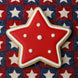 Star-shaped cookie with red icing and white dots on a star-patterned fabric background from a 3.5 inch Star Metal Cookie Cutter