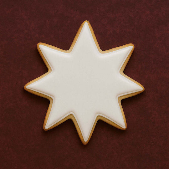 Star-shaped cookie with white icing on a dark red background from a 3.5 inch Star of Bethlehem Moravian Star Metal Cookie Cutter