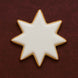 Star-shaped cookie with white icing on a dark red background from a 3.5 inch Star of Bethlehem Moravian Star Metal Cookie Cutter