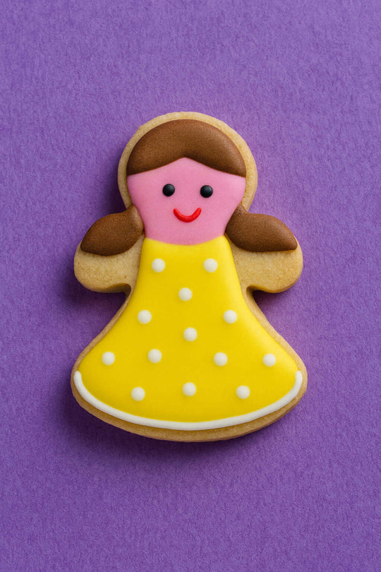 Decorative cookie shaped like a girl with a yellow dress on a purple background from a 2 inch Mini Gingerbread Girl Metal Cookie Cutter