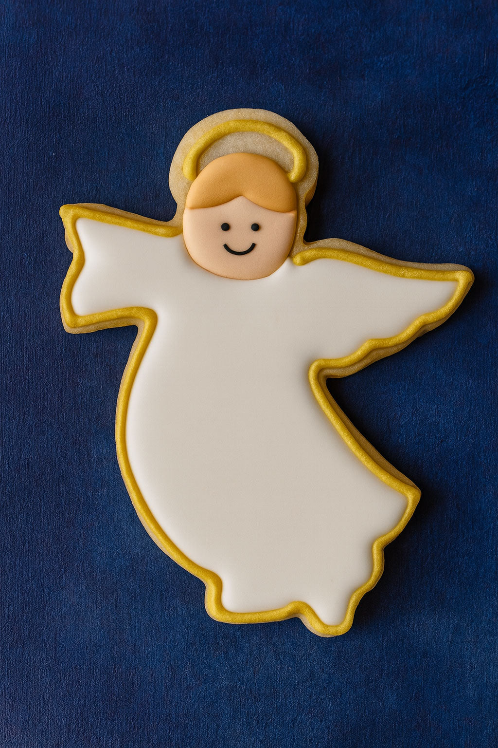Angel-shaped cookie with gold accents on a blue background from a 4.75 inch Flying Angel Metal Cookie Cutter