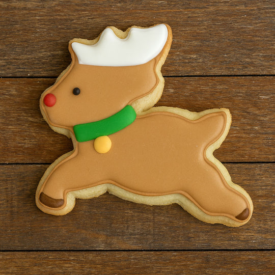 Reindeer-shaped cookie with brown body, white antlers, green nose, and red and yellow accents on a wooden surface from a 3 inch Reindeer Metal Cookie Cutter