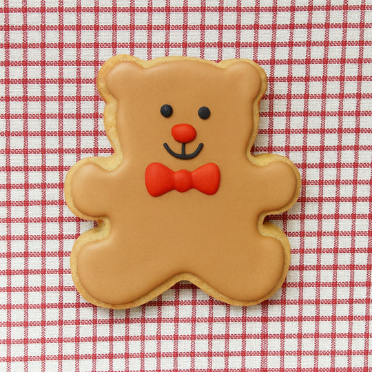 Gingerbread bear cookie with a red bow tie on a red and white checkered background from a 3 inch Teddy Bear Metal Cookie Cutter