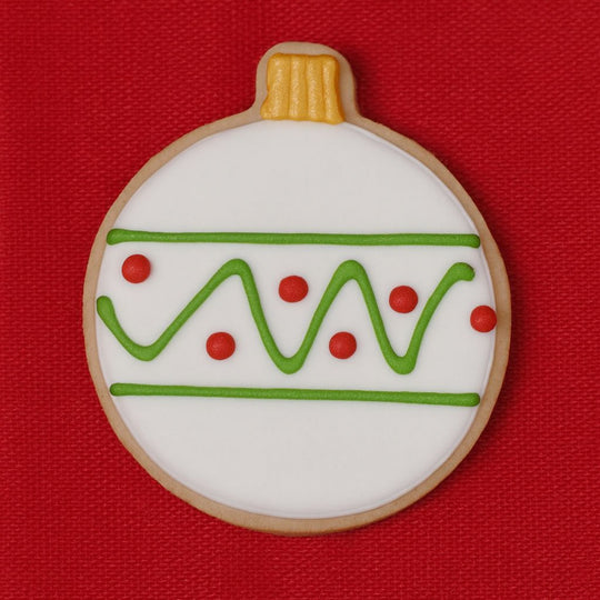 Decorative cookie shaped like a Christmas ornament with green and red icing on a red background from a 3 inch Ornament or Fishing Bobber Metal Cookie Cutter
