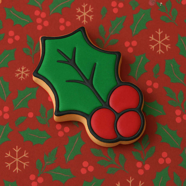 3 inch Holly Leaf Metal Cookie Cutter shaped cookie decorated in green and red on festive background.