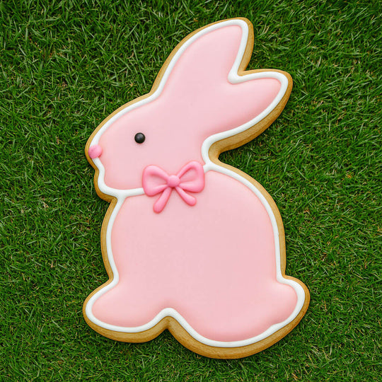 3.25 inch Chocolate Easter Bunny Rabbit Metal Cookie Cutter shaped cookie decorated in pink icing with a bow on grass.